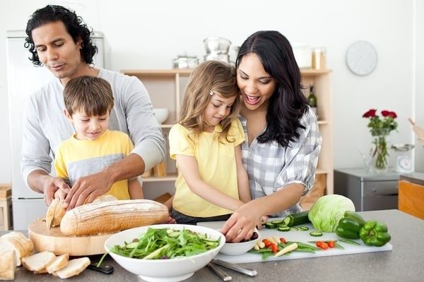 Barnfamilj lagar mat tillsammans med grönsaker och bröd i köket