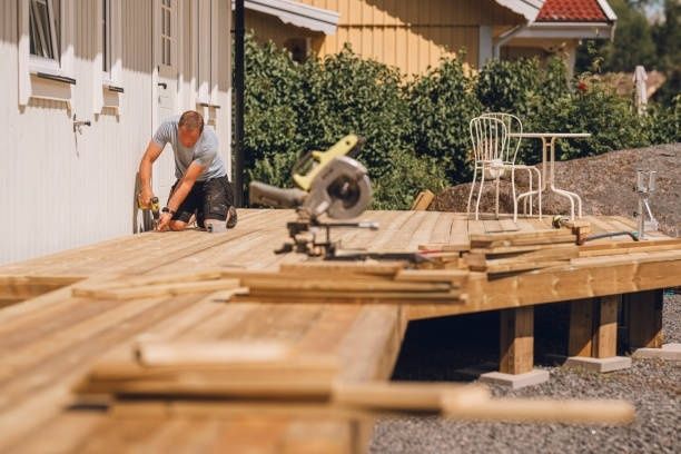 Person bygger ett trädäck med virke och verktyg i en trädgård